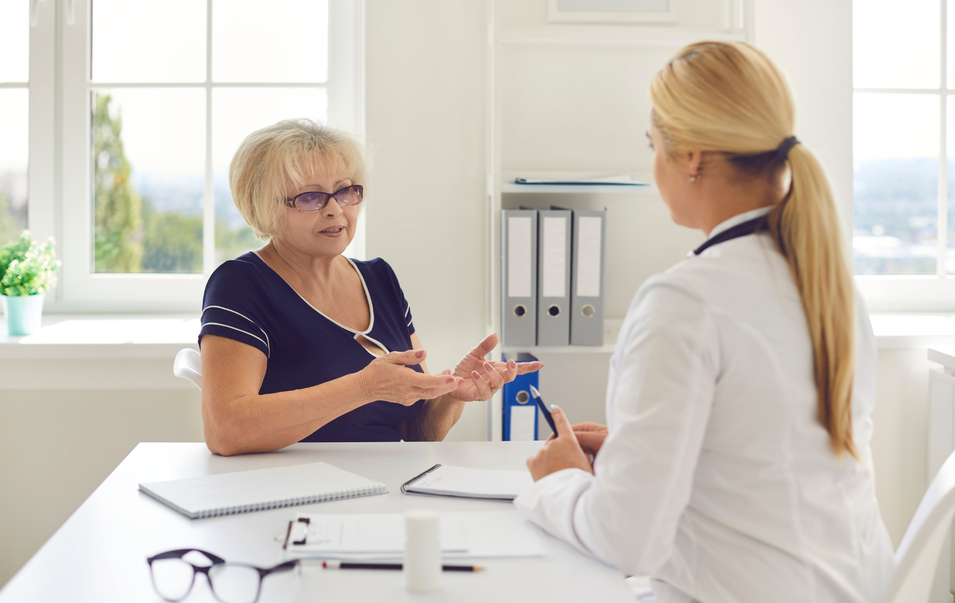 Doctor speaking with a patient across a desk in a bright clinic office