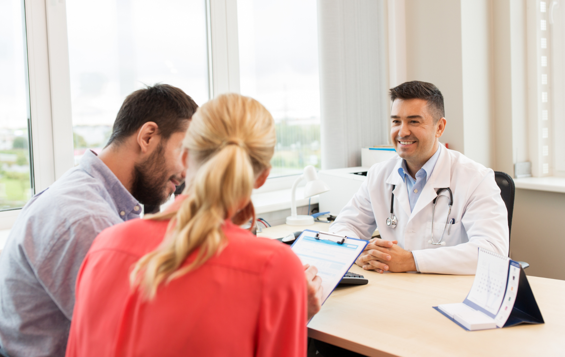Doctor meeting with two clients at a desk, discussing documents in a bright office