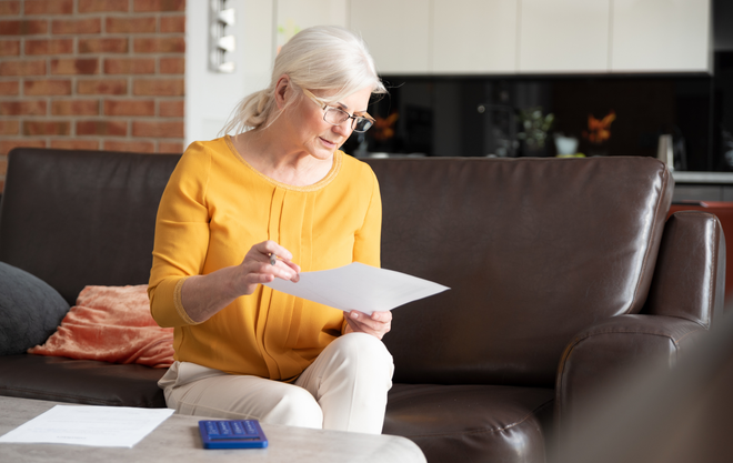 Woman in a yellow sweater reading a paper on a brown sofa in a living room