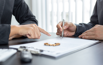 Hands reviewing and signing a document on a desk with keys in the foreground