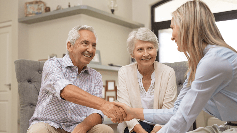 Older couple shaking hands with a caregiver in a bright living room