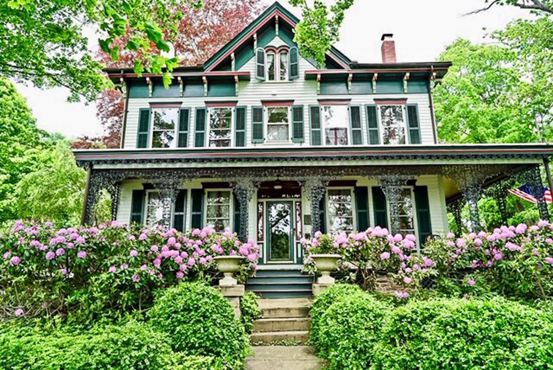 A large white and green house with purple flowers in front of it.