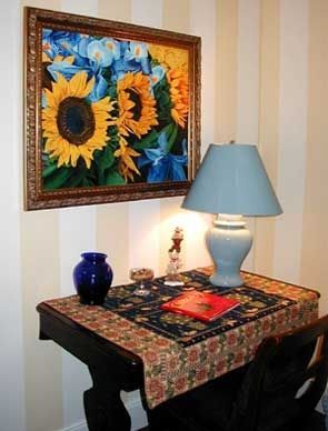 A painting of sunflowers hangs above a table with a lamp