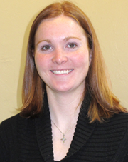A woman wearing a black sweater and a cross necklace smiles for the camera.
