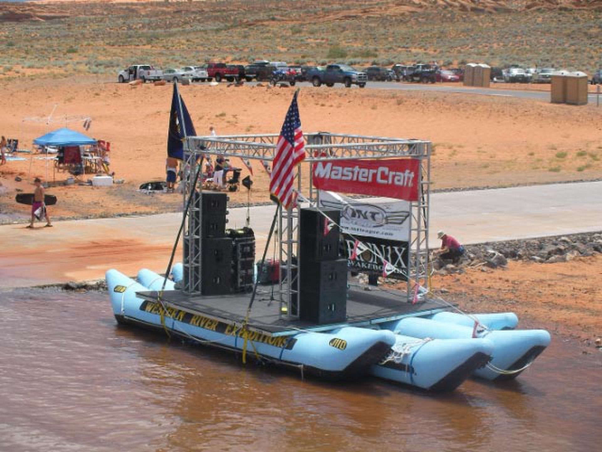 A concert stage built on a J-Rig raft beside parked vehicles