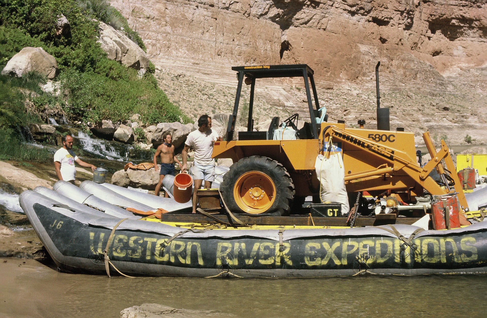 A backhoe rests on a Western River Expeditions J-Rig beside the riverbank