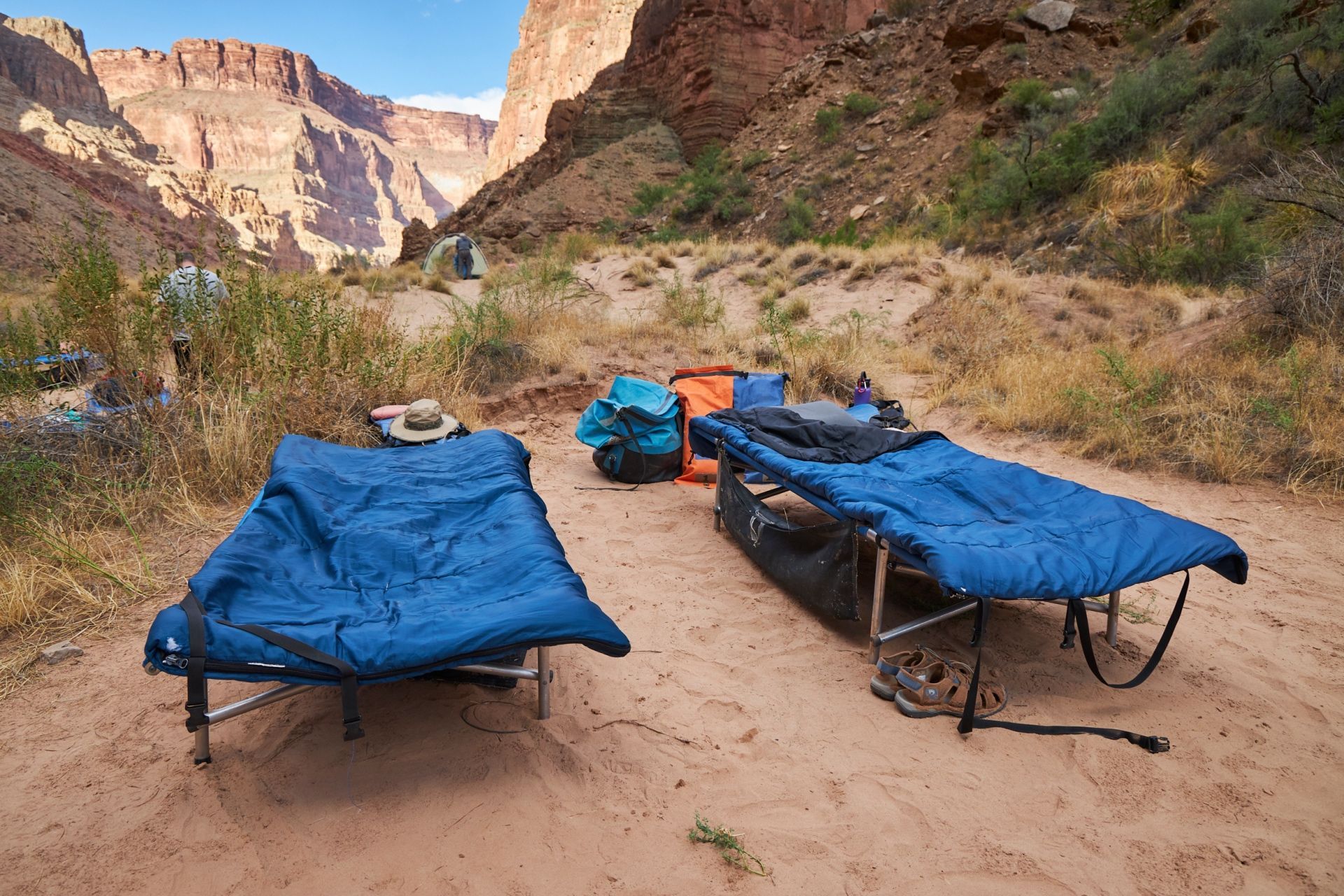 Cots and sleeping bags arranged on a sandy canyon beach