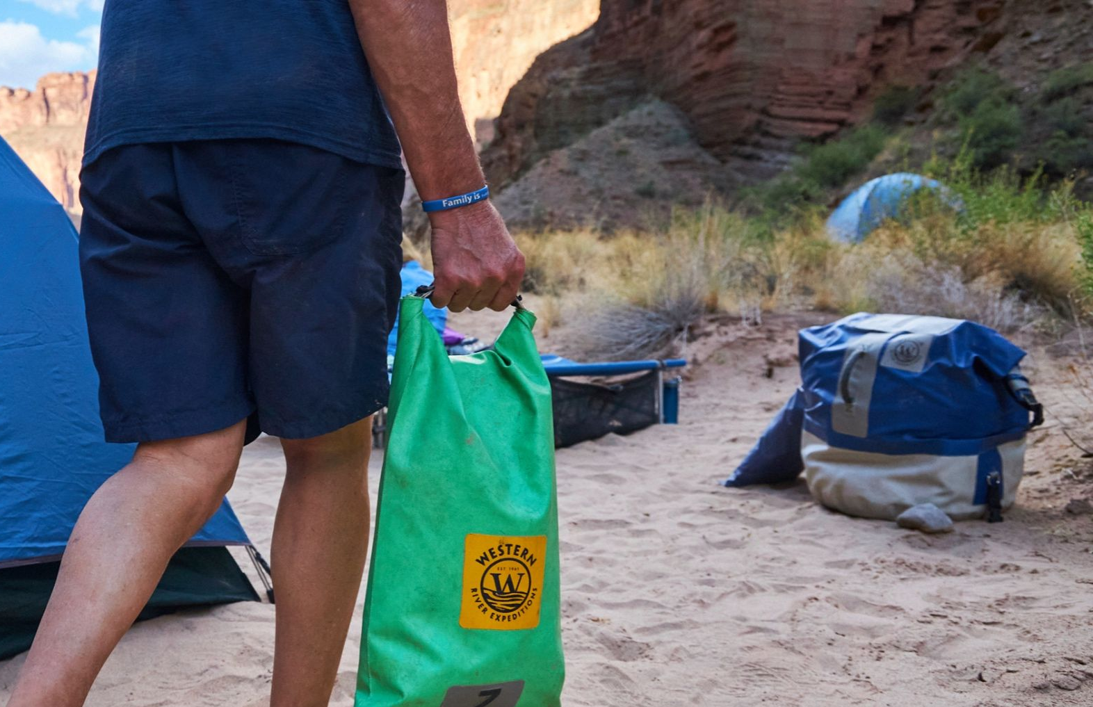A person walking across the sand holding a dry bag.