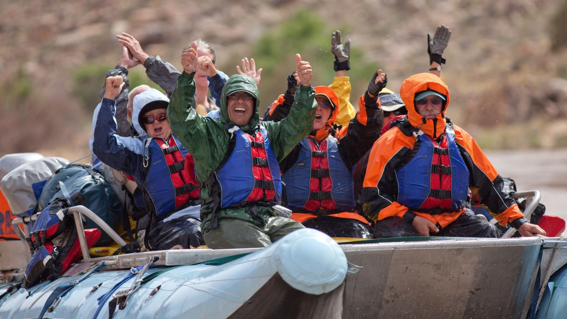 A group of people on a raft wearing rain gear and life jackets.