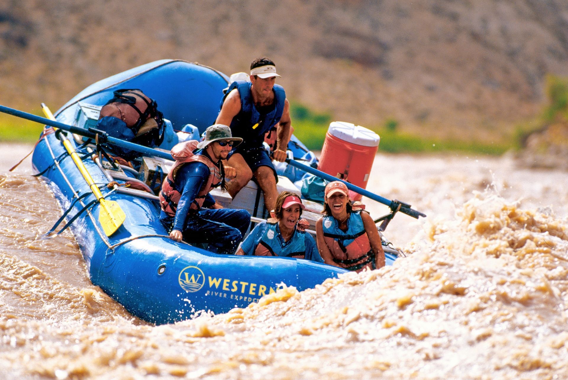 Blue raft carrying guests through a Cataract Canyon rapid