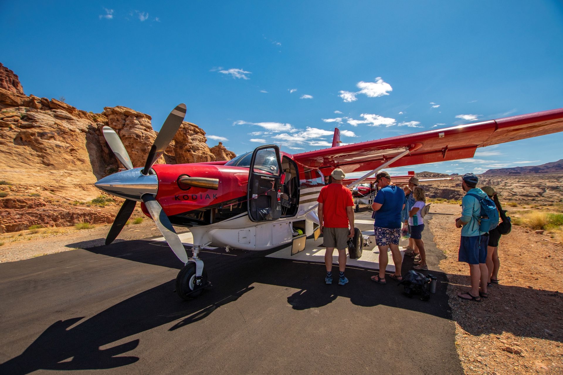 Guests stand beside a small plane at a canyon airstrip