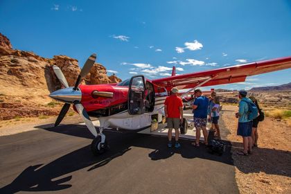 A red and white prop plane on a runway with guests loading from the side.