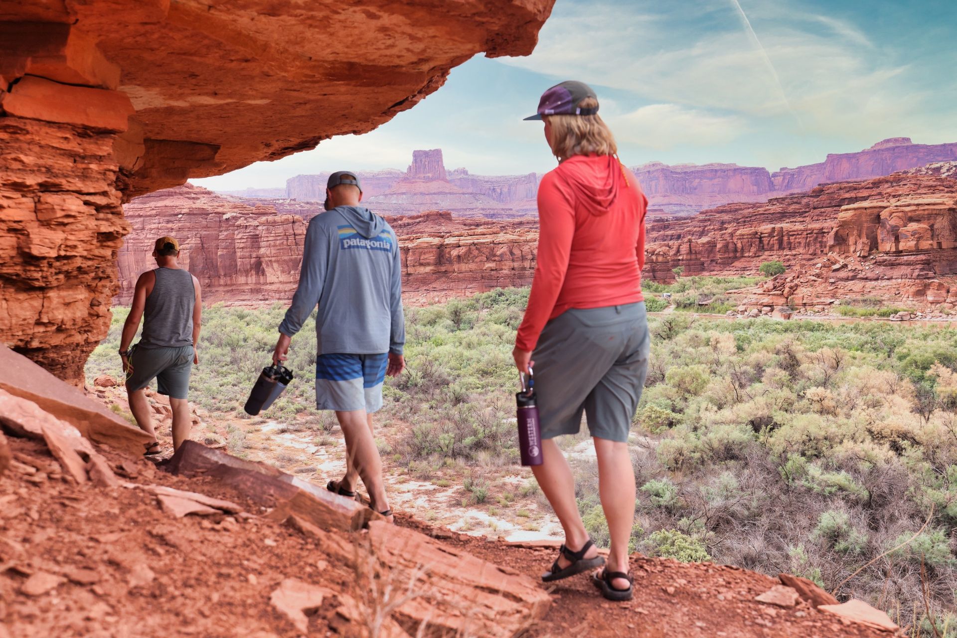 Hikers carrying water bottles beneath a red-rock overhang in Cataract Canyon