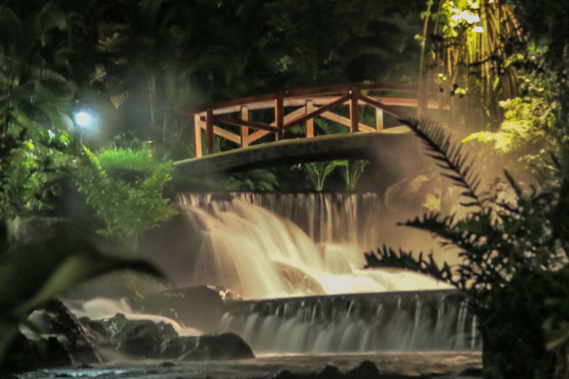 Illuminated wooden footbridge over a stream at night