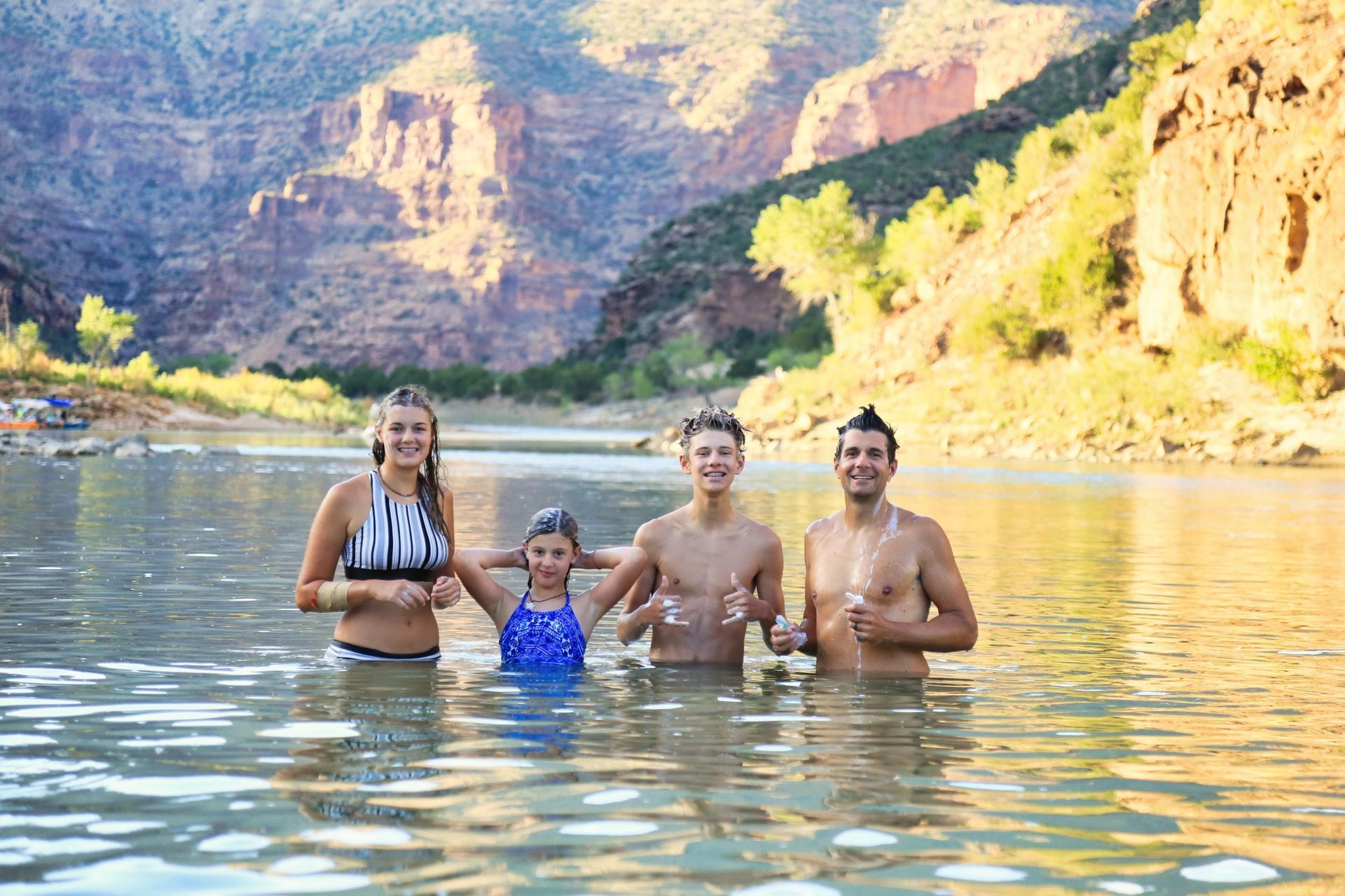 A family wades in calm water below the canyon cliffs
