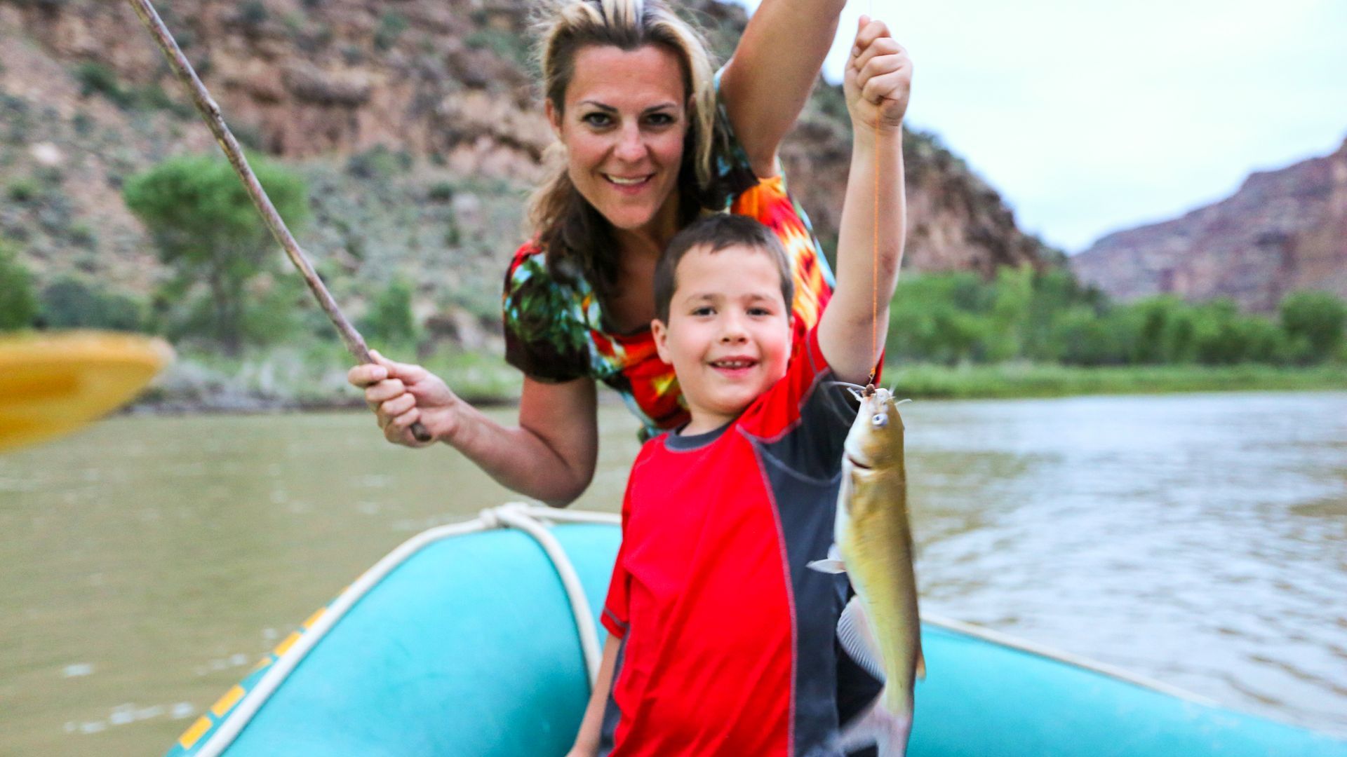 An adult and child hold up a fish beside their raft