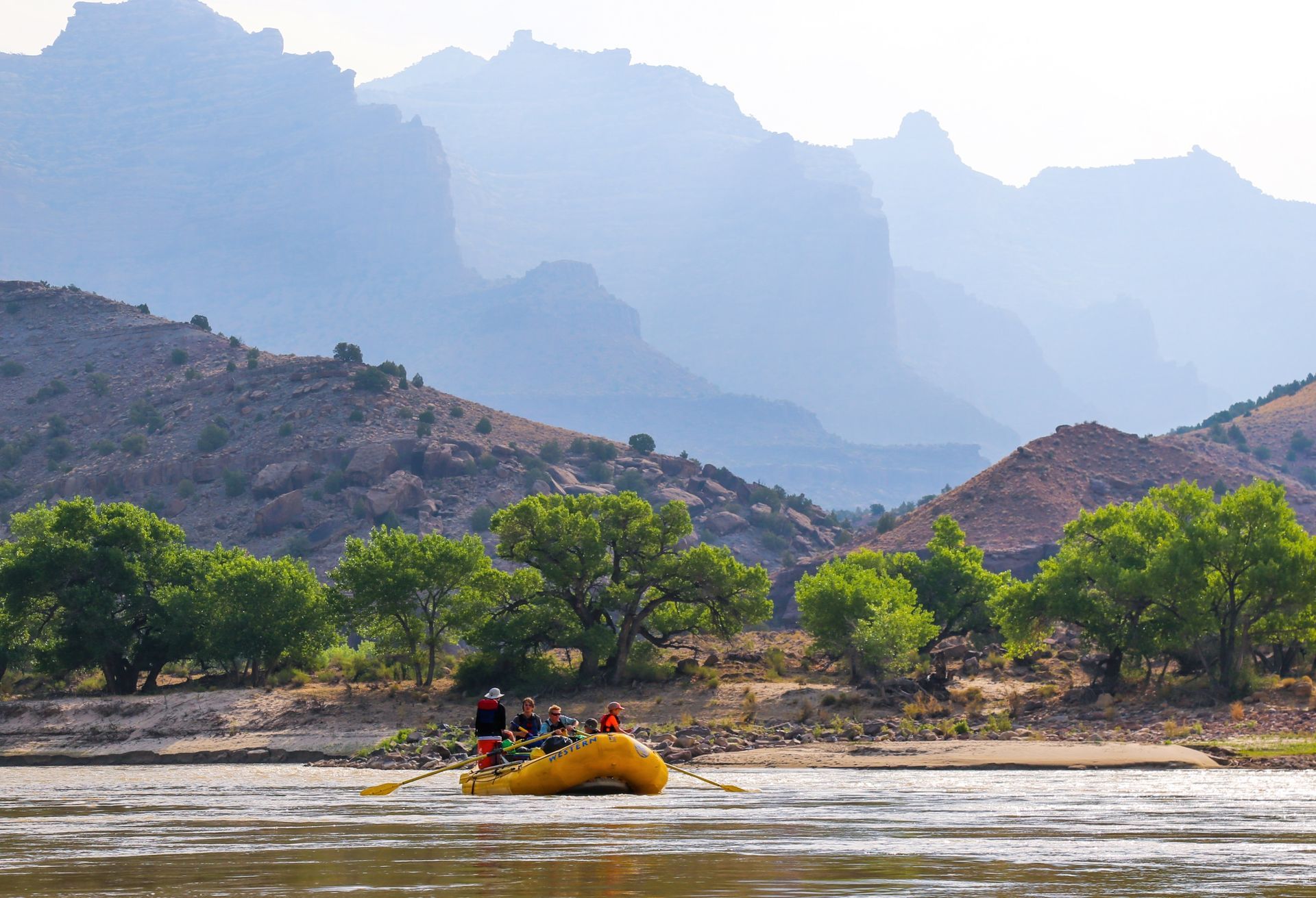 A raft floats beneath Desolation Canyon’s layered cliffs