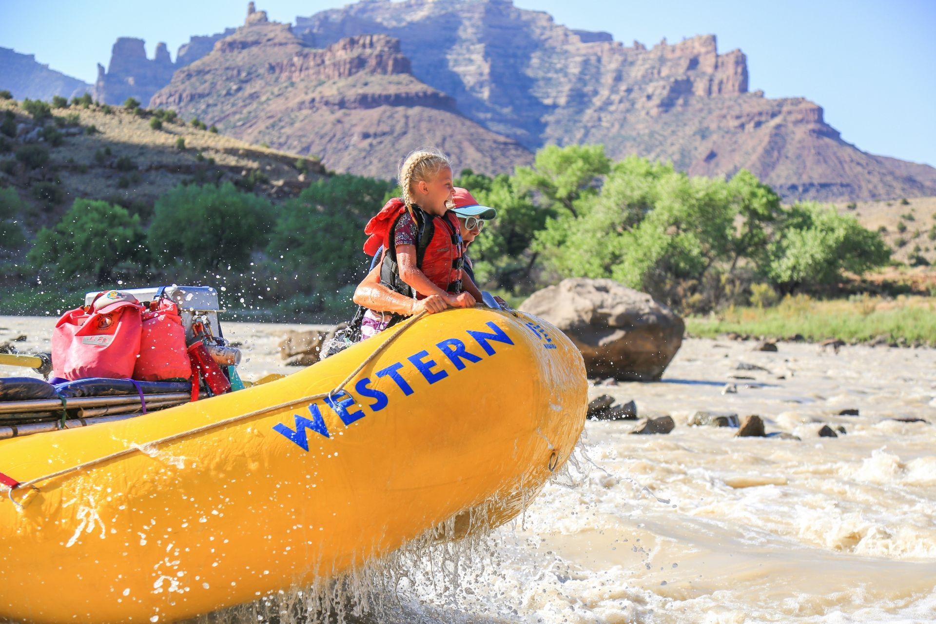 Two guests ride at the front of a yellow oar raft in Desolation Canyon