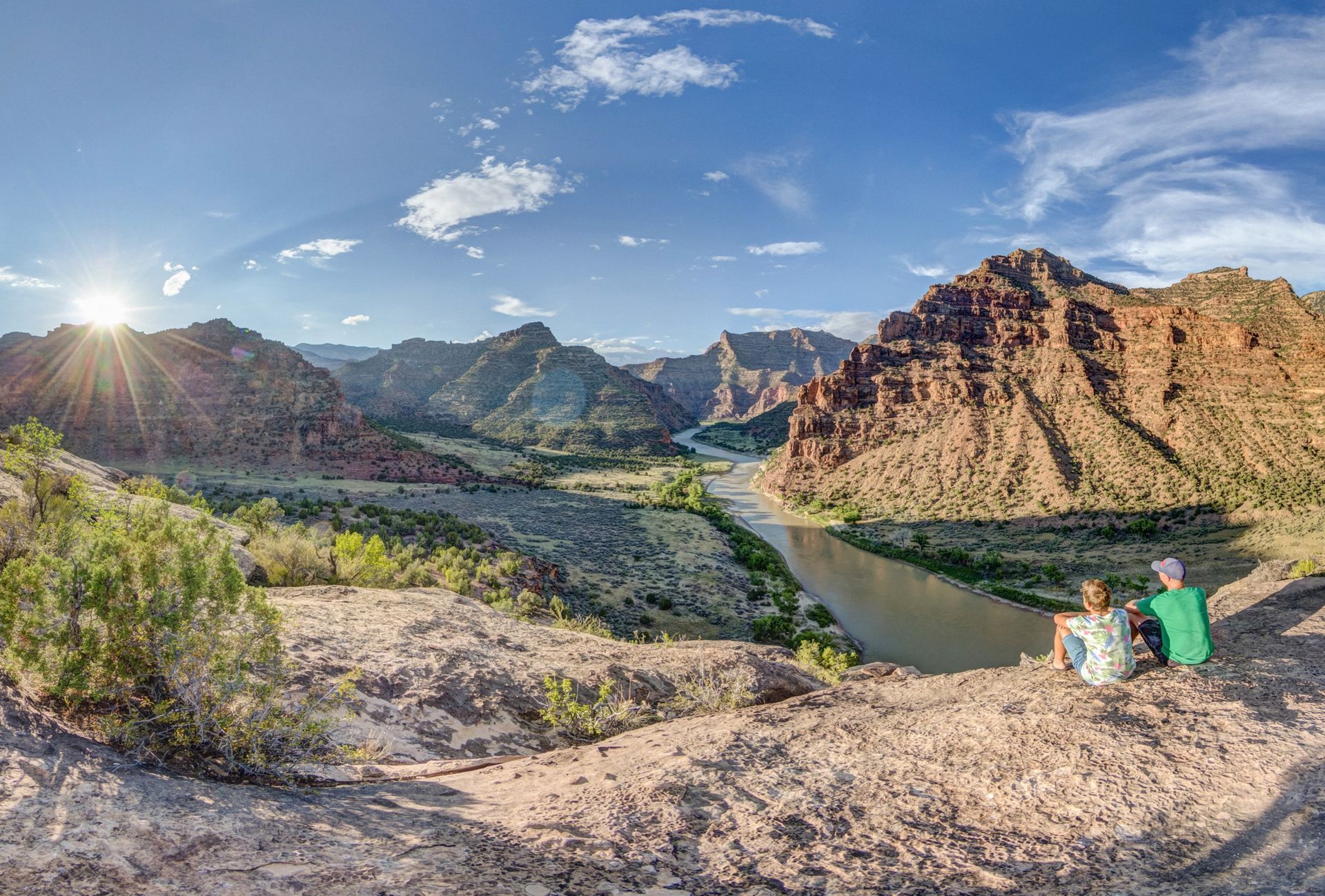 Two people overlook a bend in the Green River from a canyon ledge