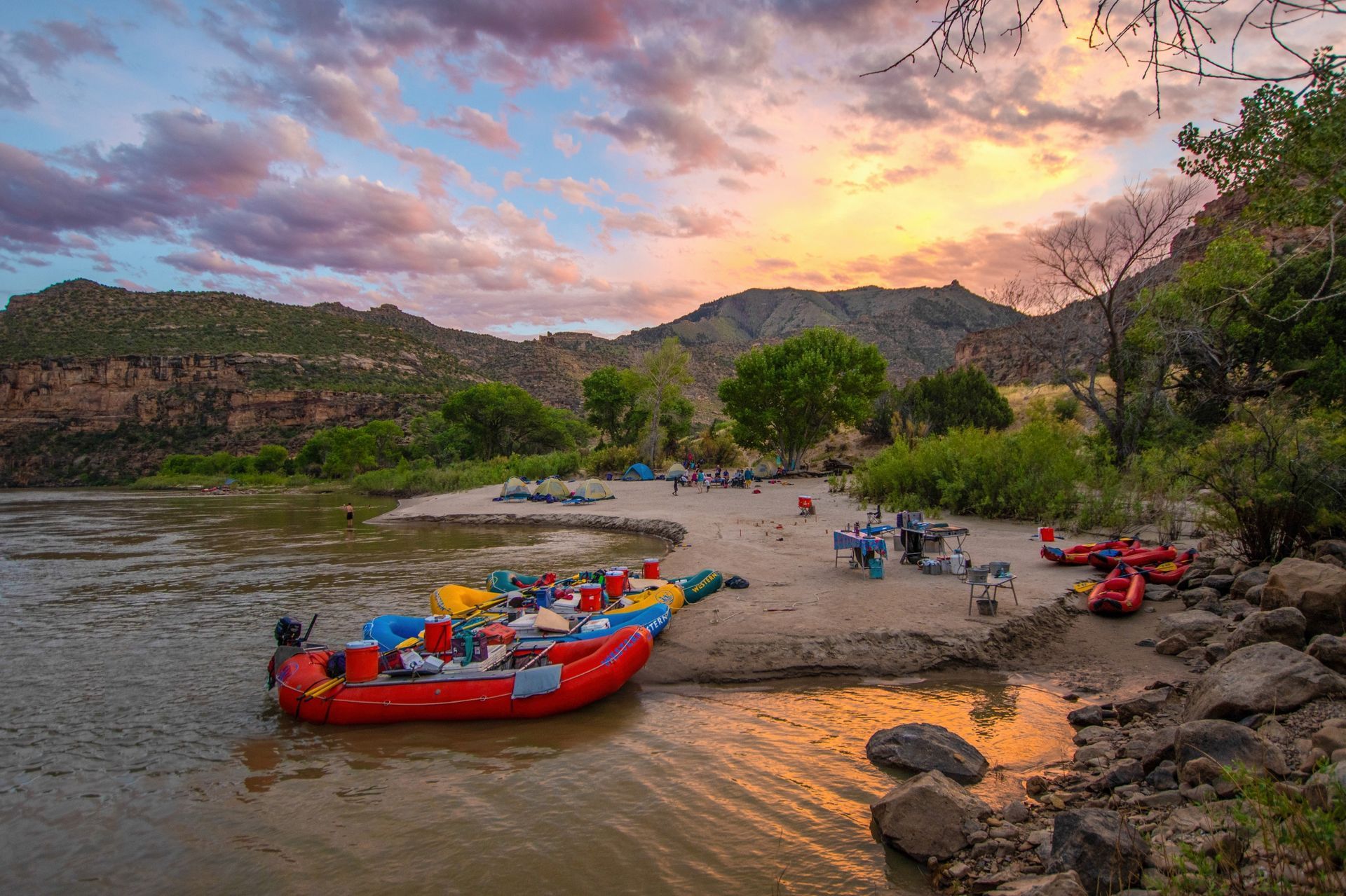 Rafts moored beside a sandy river camp at sunset