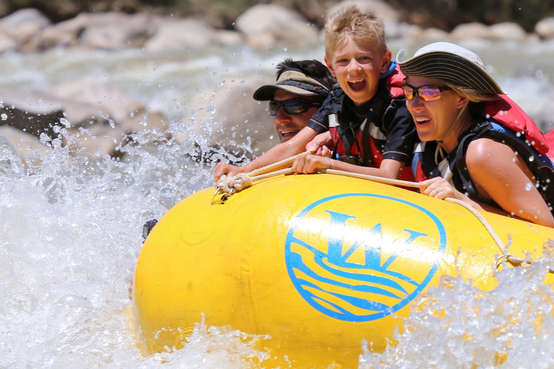 Family riding a yellow raft through splashing whitewater rapids in Desolation Canyon