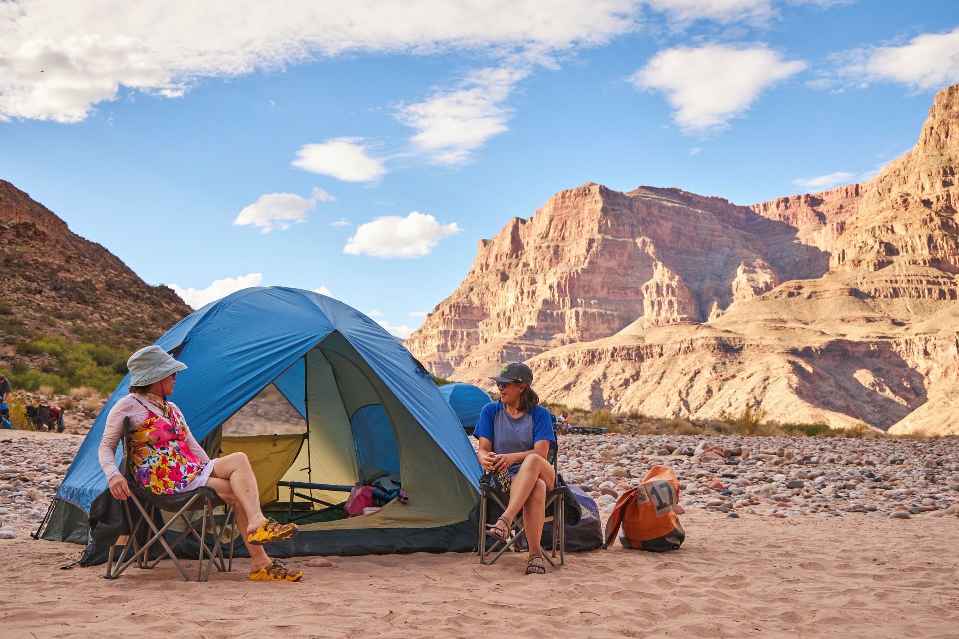 Campers sit beside a blue tent on a sandy Grand Canyon beach