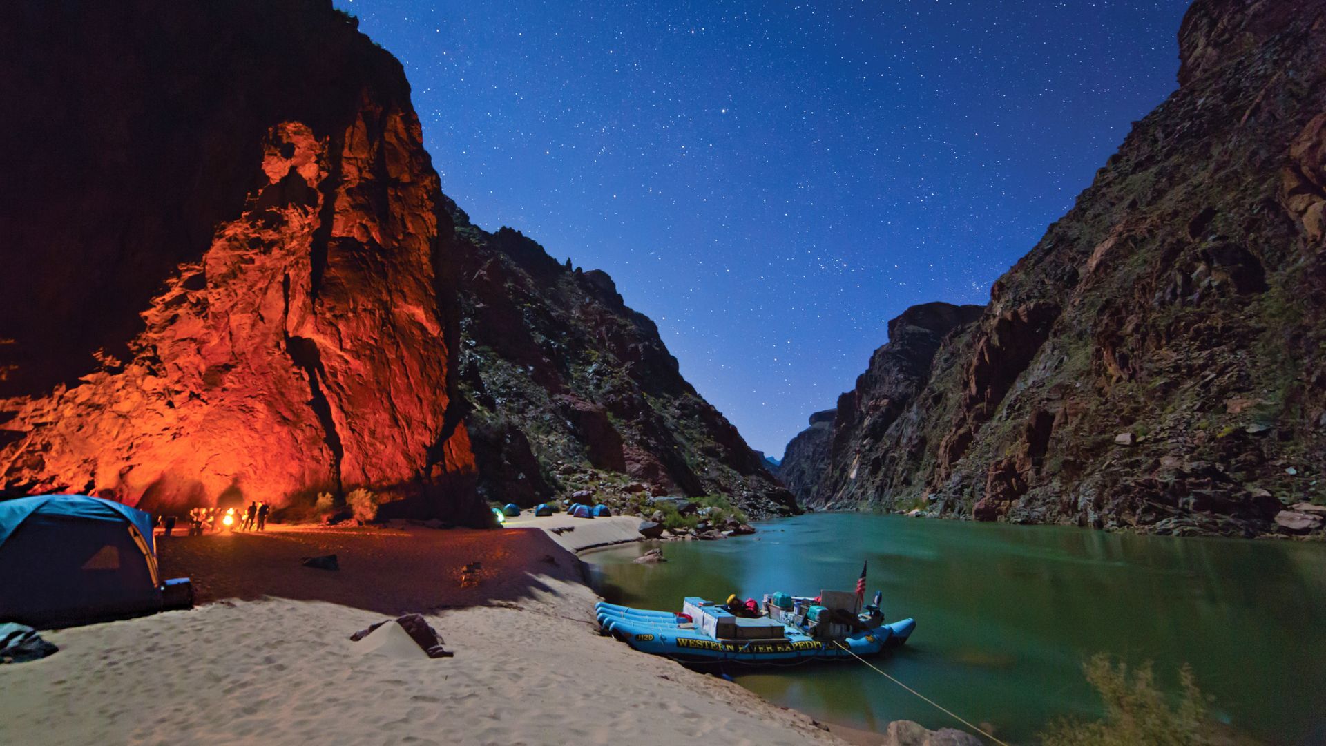 A campfire lights a canyon wall beside the Colorado River at night