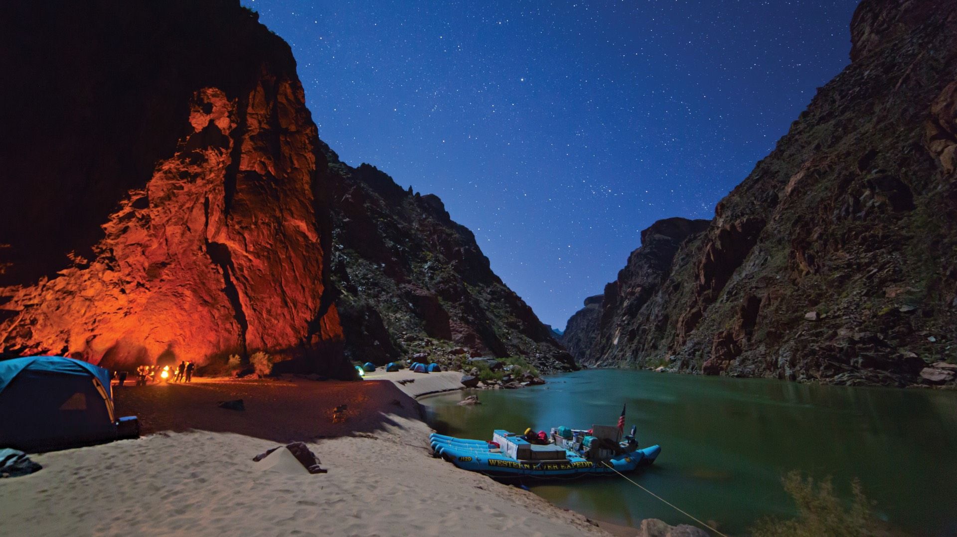 A campfire lights a canyon wall beside the Colorado River at night