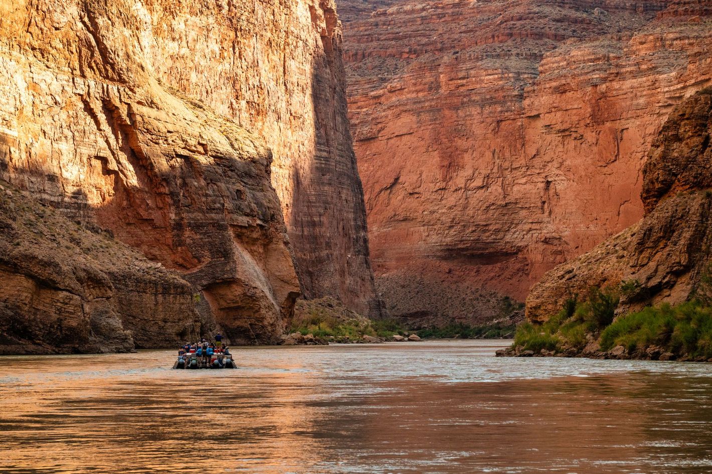 A raft floats beneath shaded Grand Canyon walls