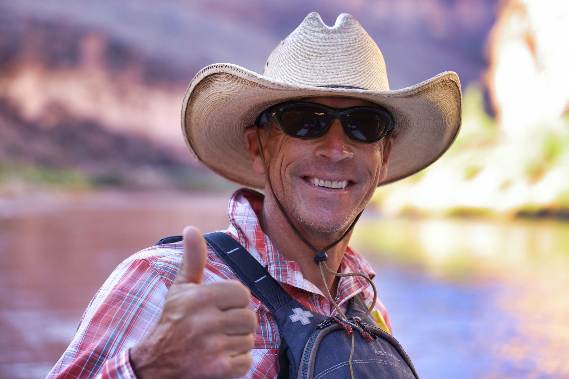A river guide with a cowboy hat on smiles with a thumbs up. 
