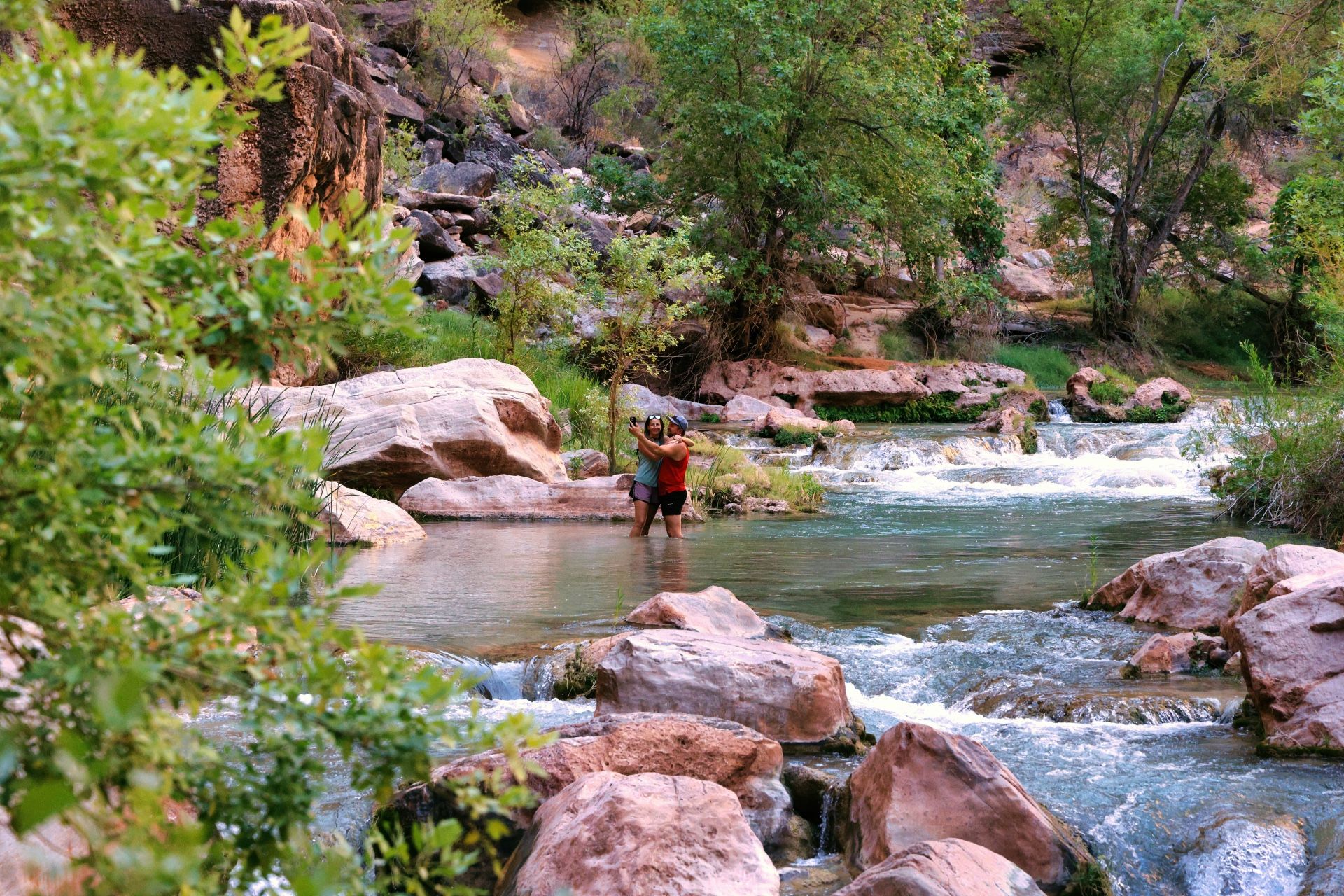 Two hikers take a photograph beside a rocky creek