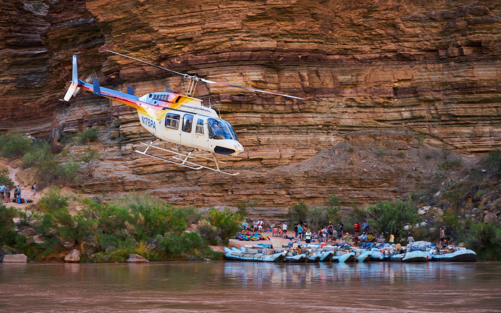 A helicopter flies above rafts moored beside the Colorado River