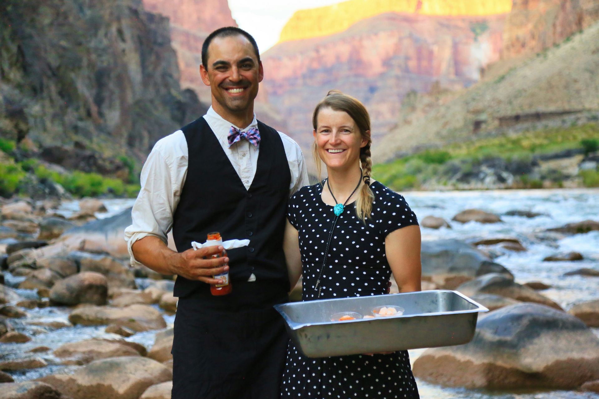 Two guides hold a serving tray beside the river
