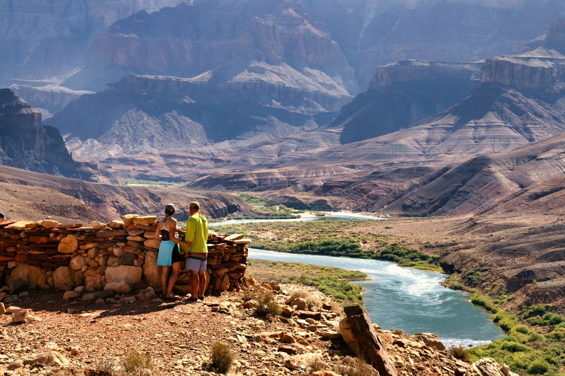 Two hikers stand beside stone ruins above a river bend