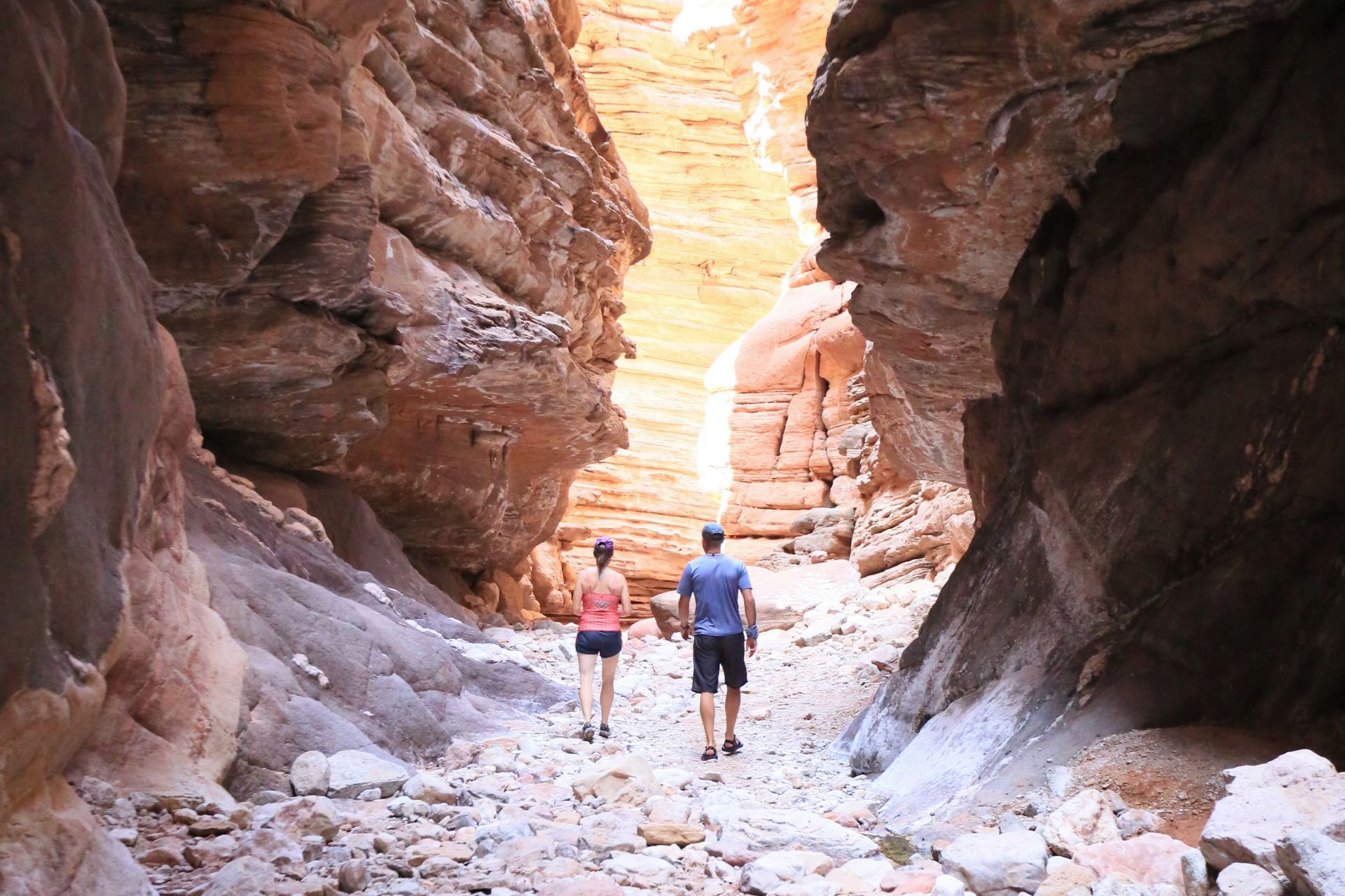 Two hikers walk through a narrow sandstone canyon
