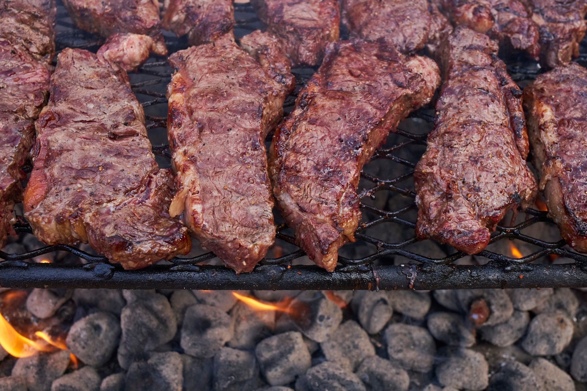 Steaks cooking on a grill over coals