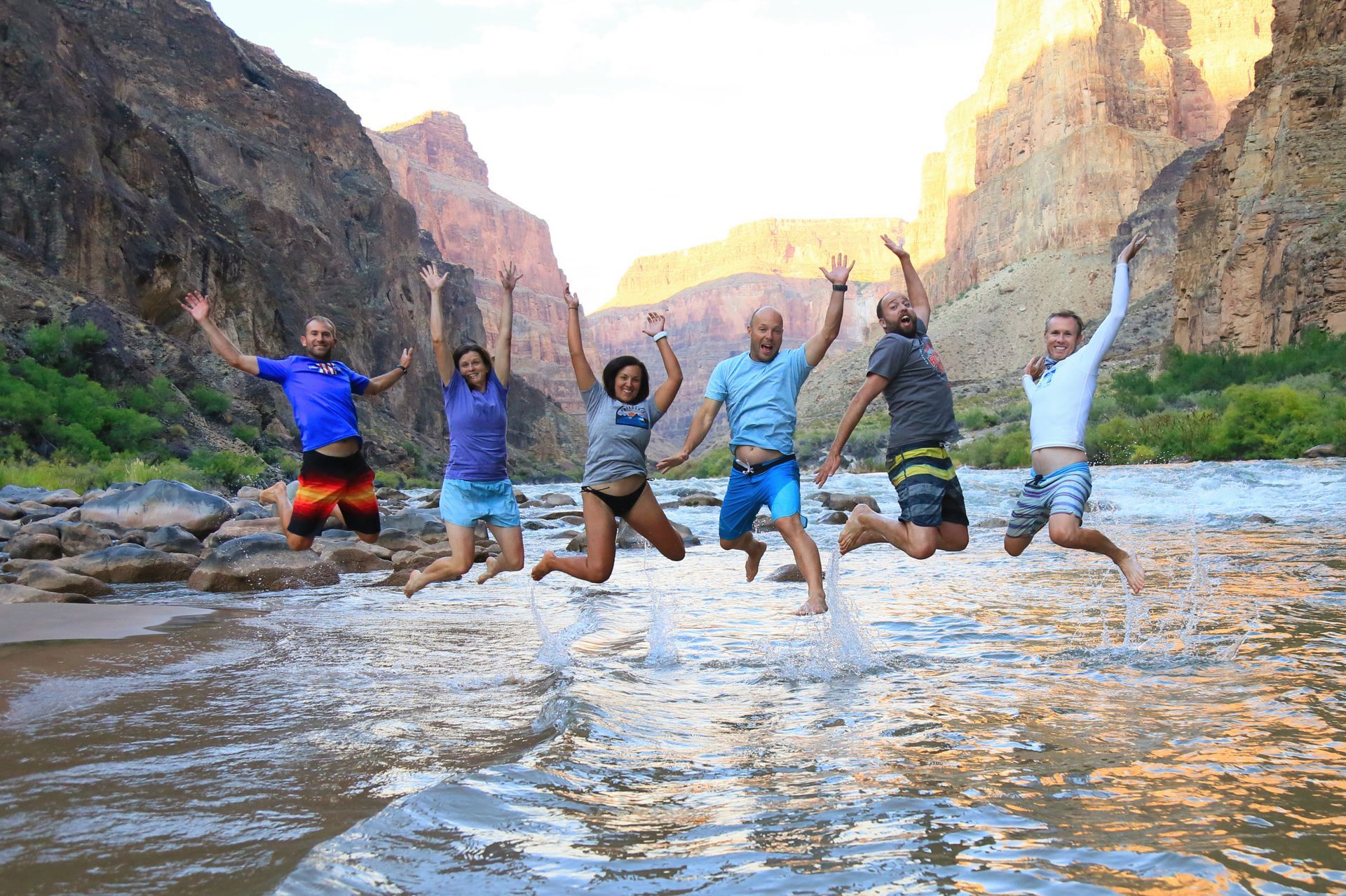 A group jumping in shallow water between Grand Canyon walls