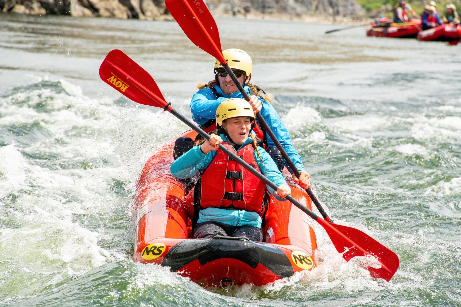An adult and child paddle an inflatable kayak through whitewater