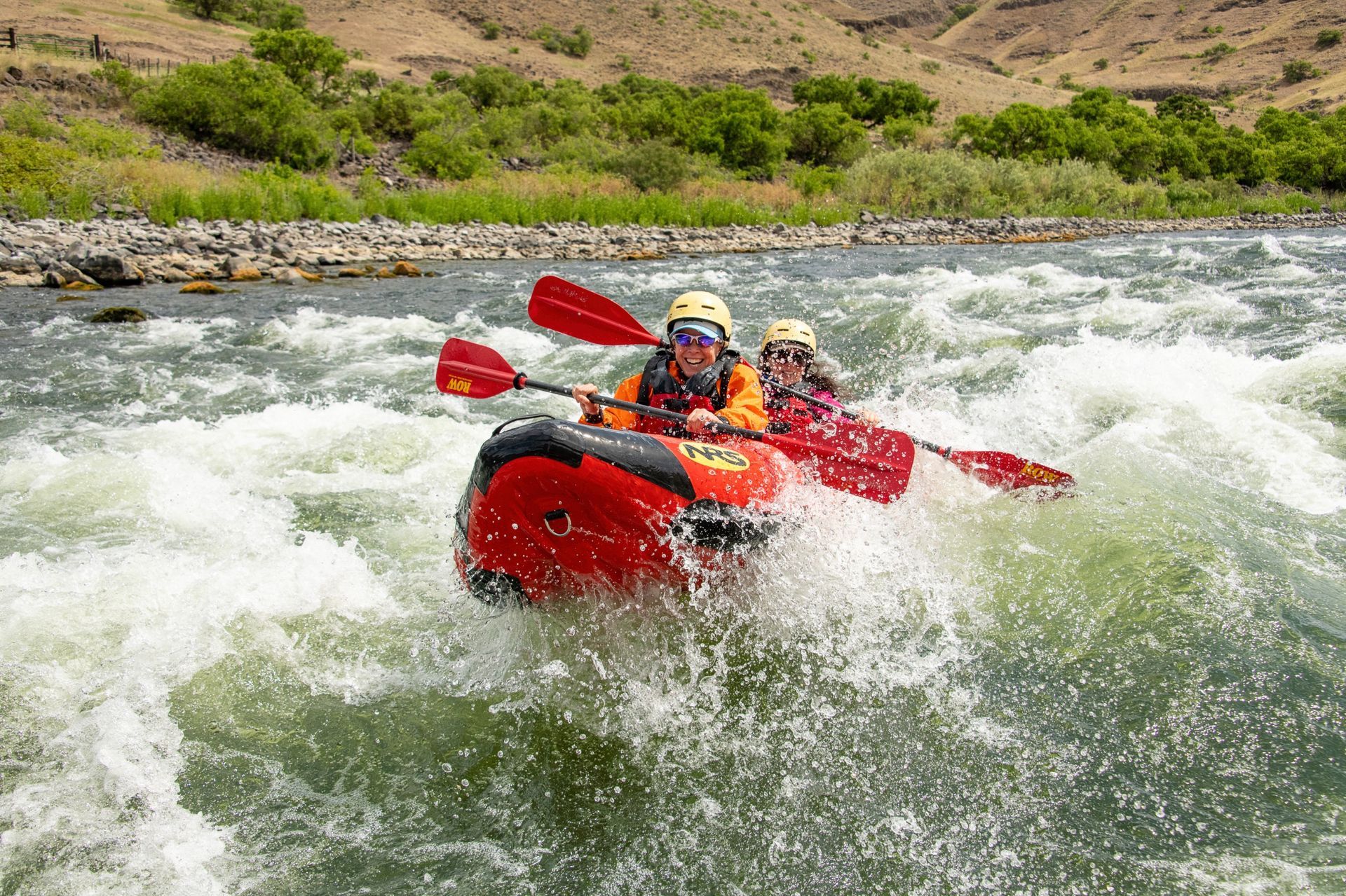 Two kayakers paddle through a whitewater wave in Hells Canyon