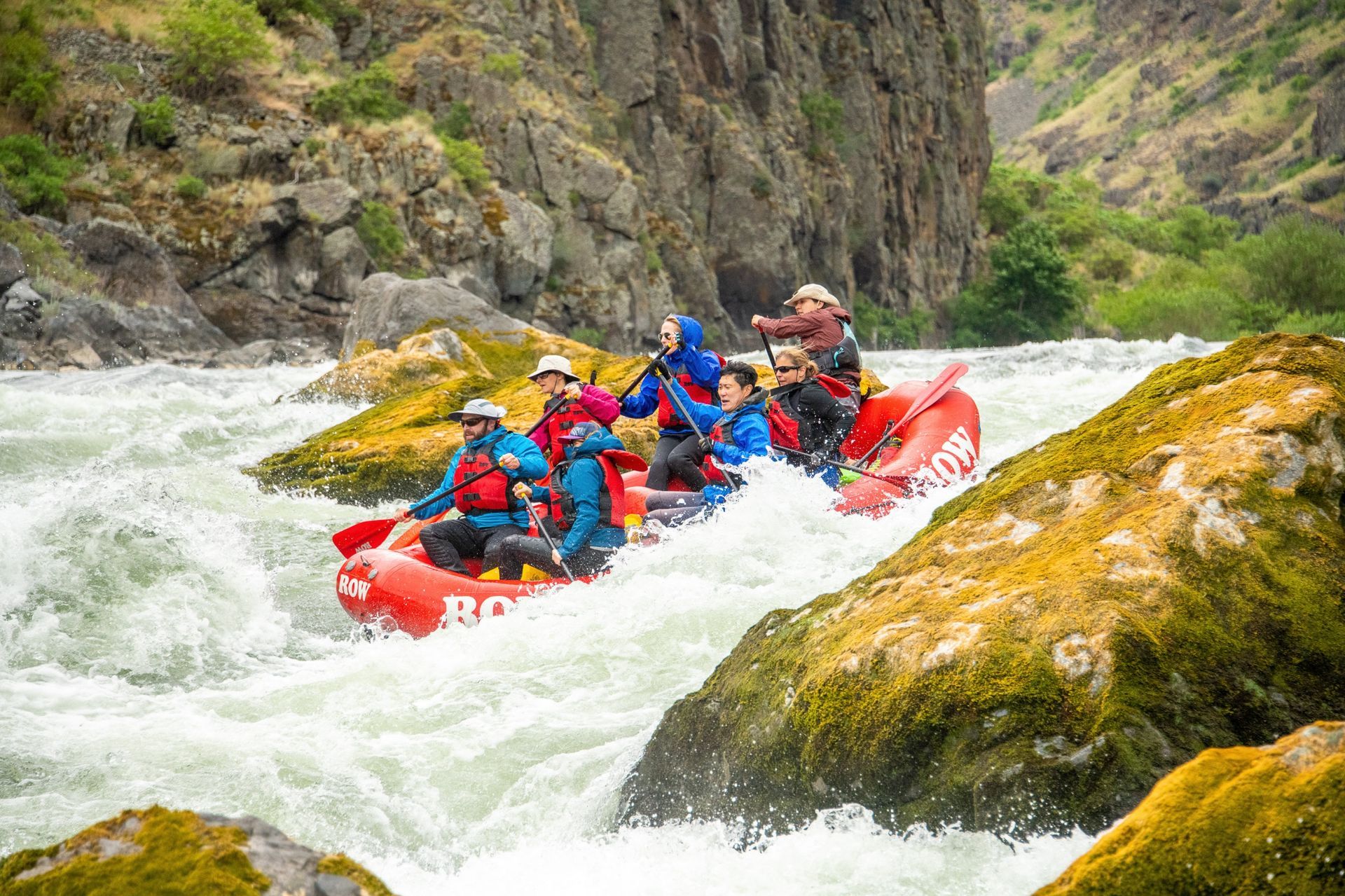 A red raft passes moss-covered rocks in Hells Canyon whitewater