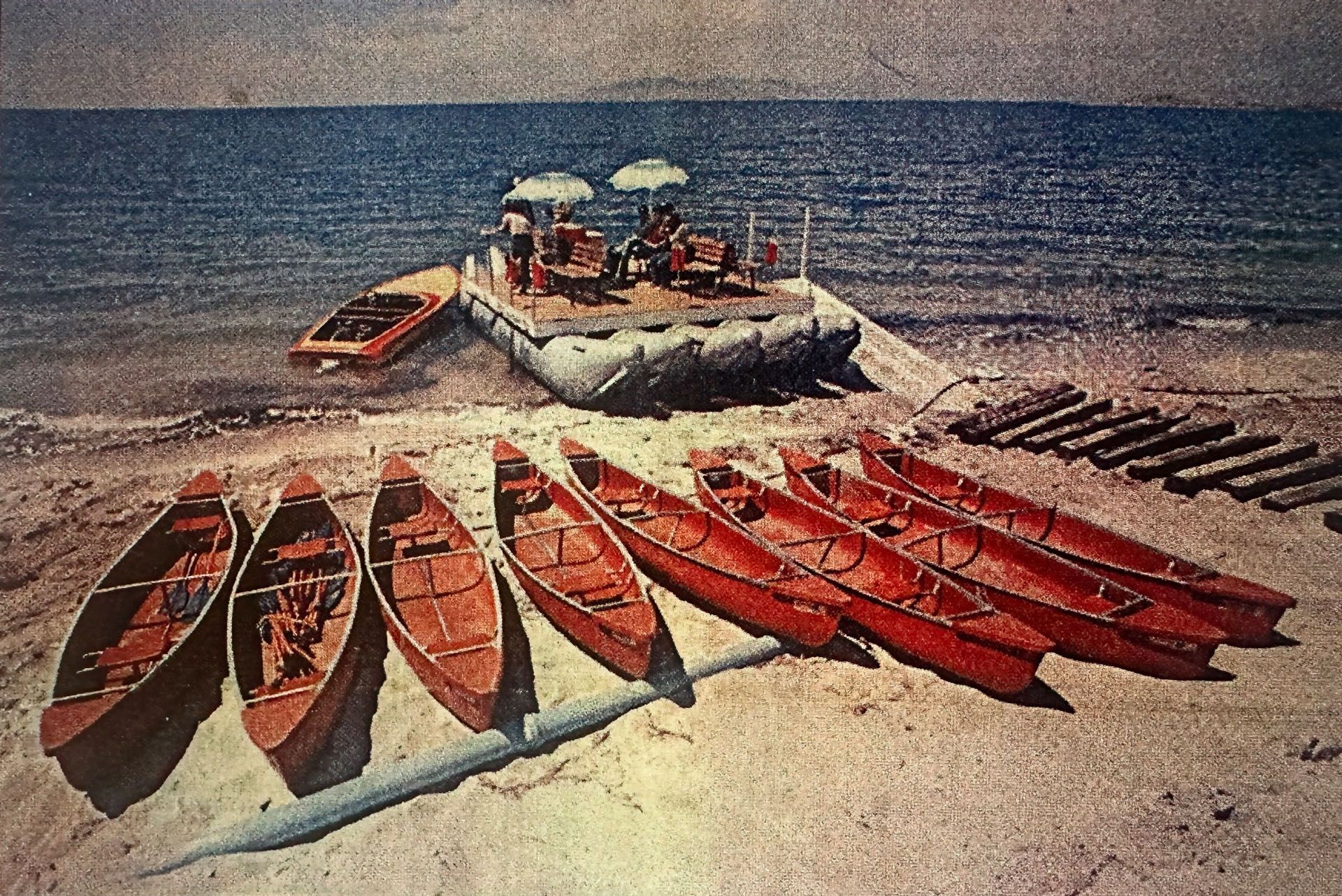A J-Rig loaded with passengers sits offshore beside red kayaks and boats