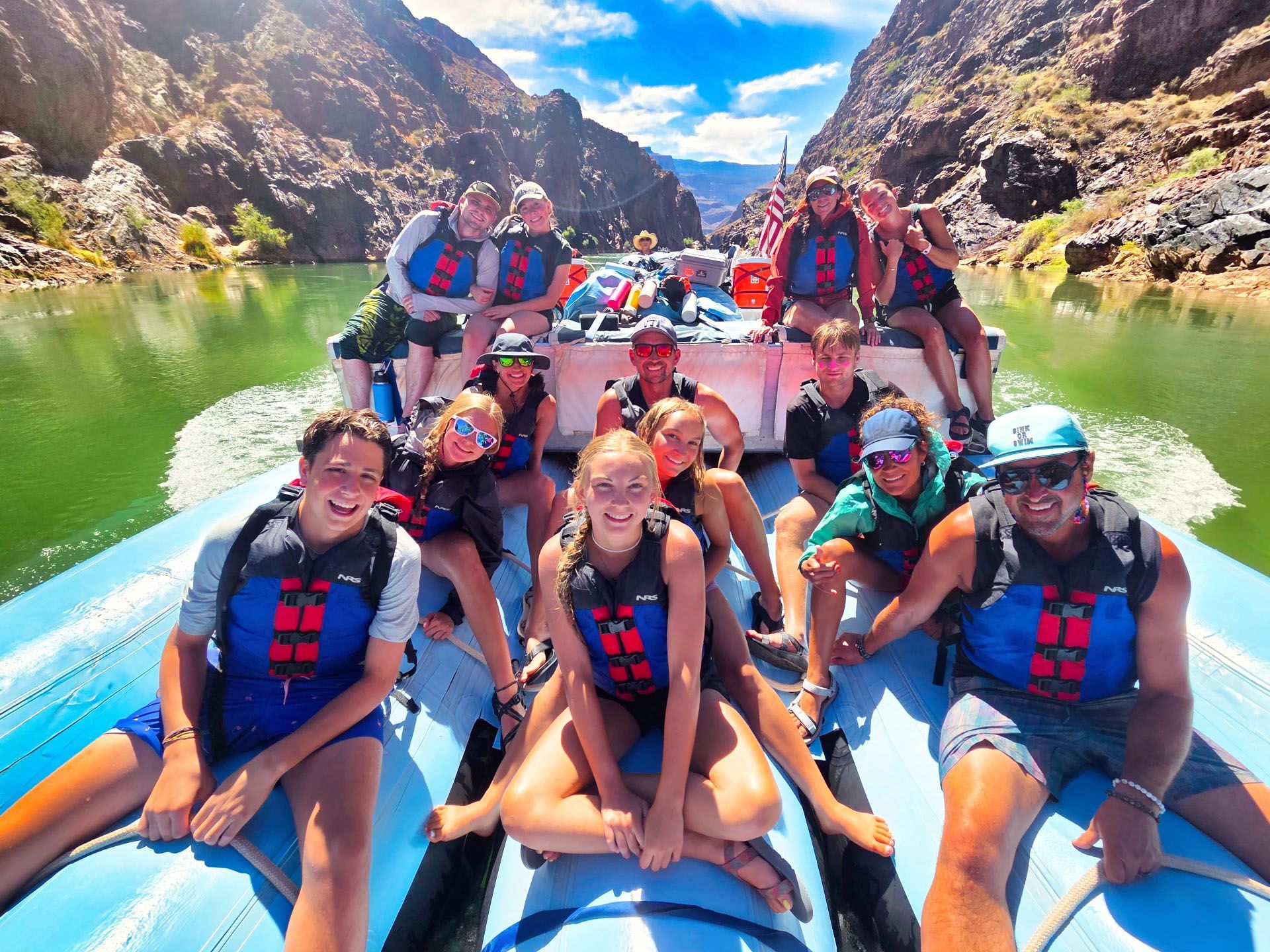 A group of people sit on a J-Rig raft, smiling and relaxing on a calm stretch of river. 