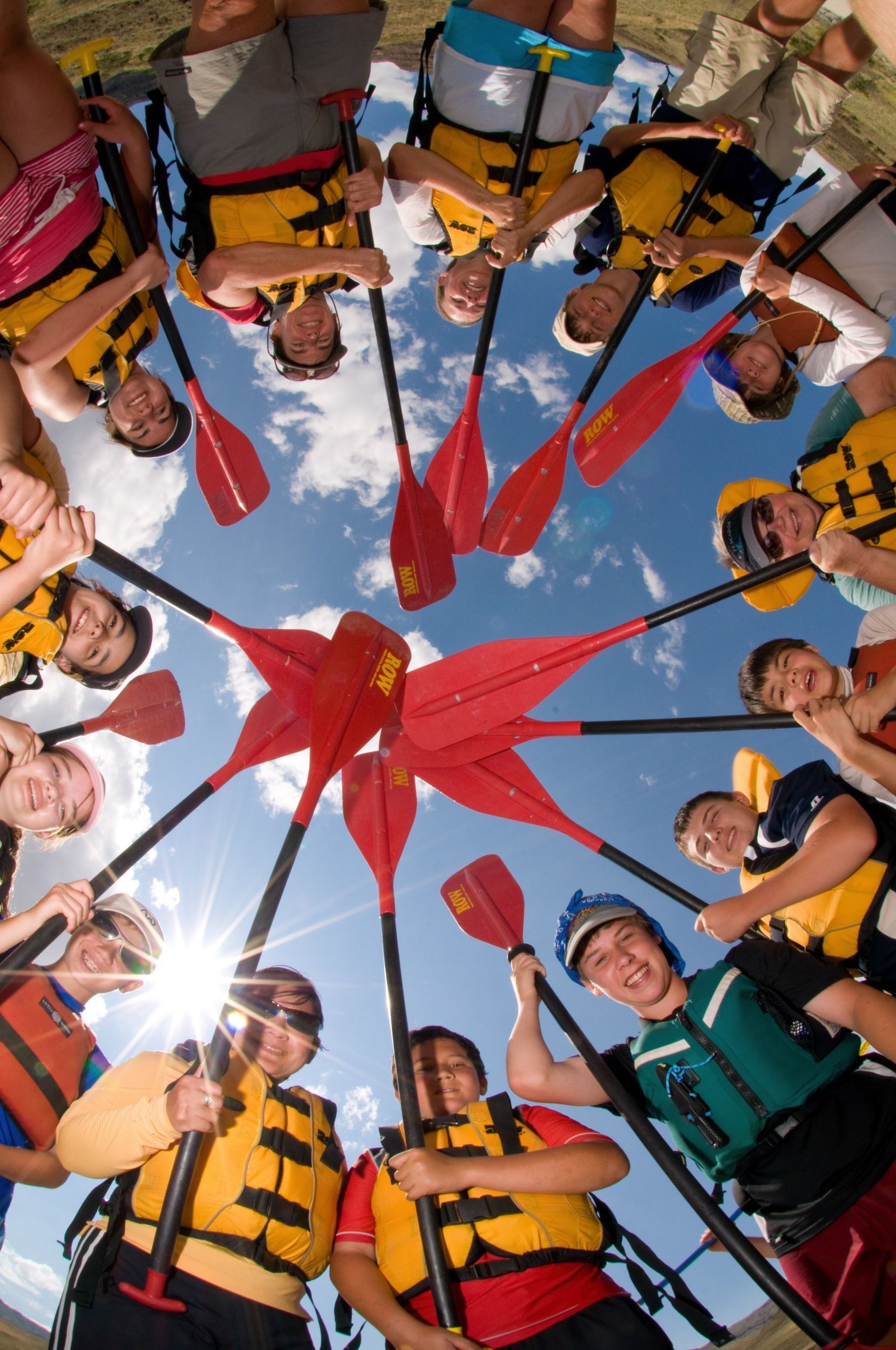 Rafters form a circle and lift their paddles toward the camera