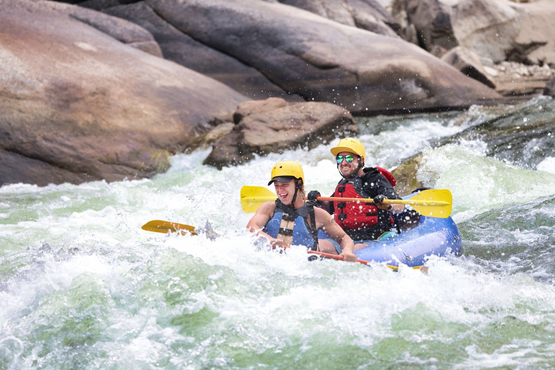 Two kayakers paddle through whitewater between large rocks