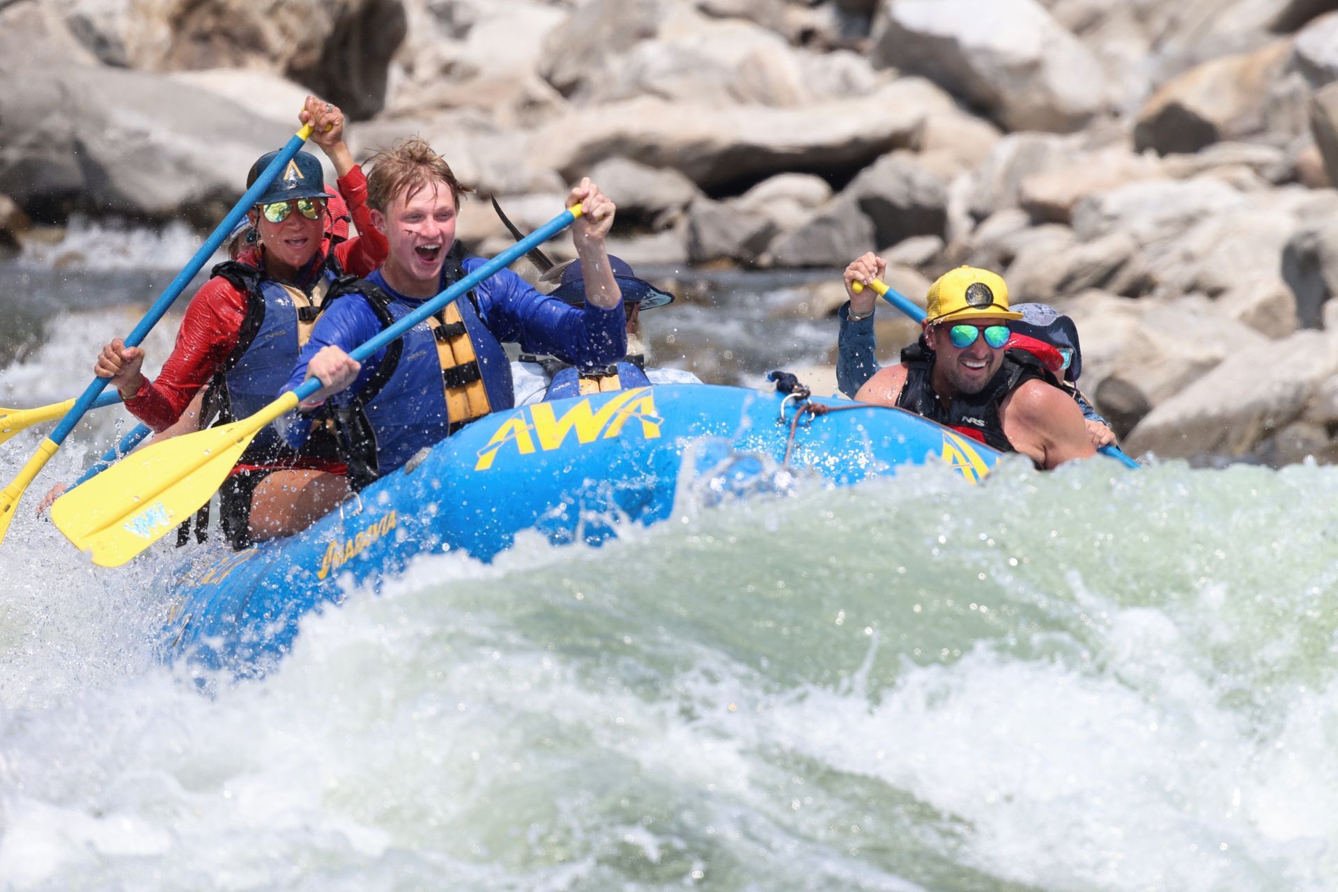 A blue paddle raft rises over a breaking wave