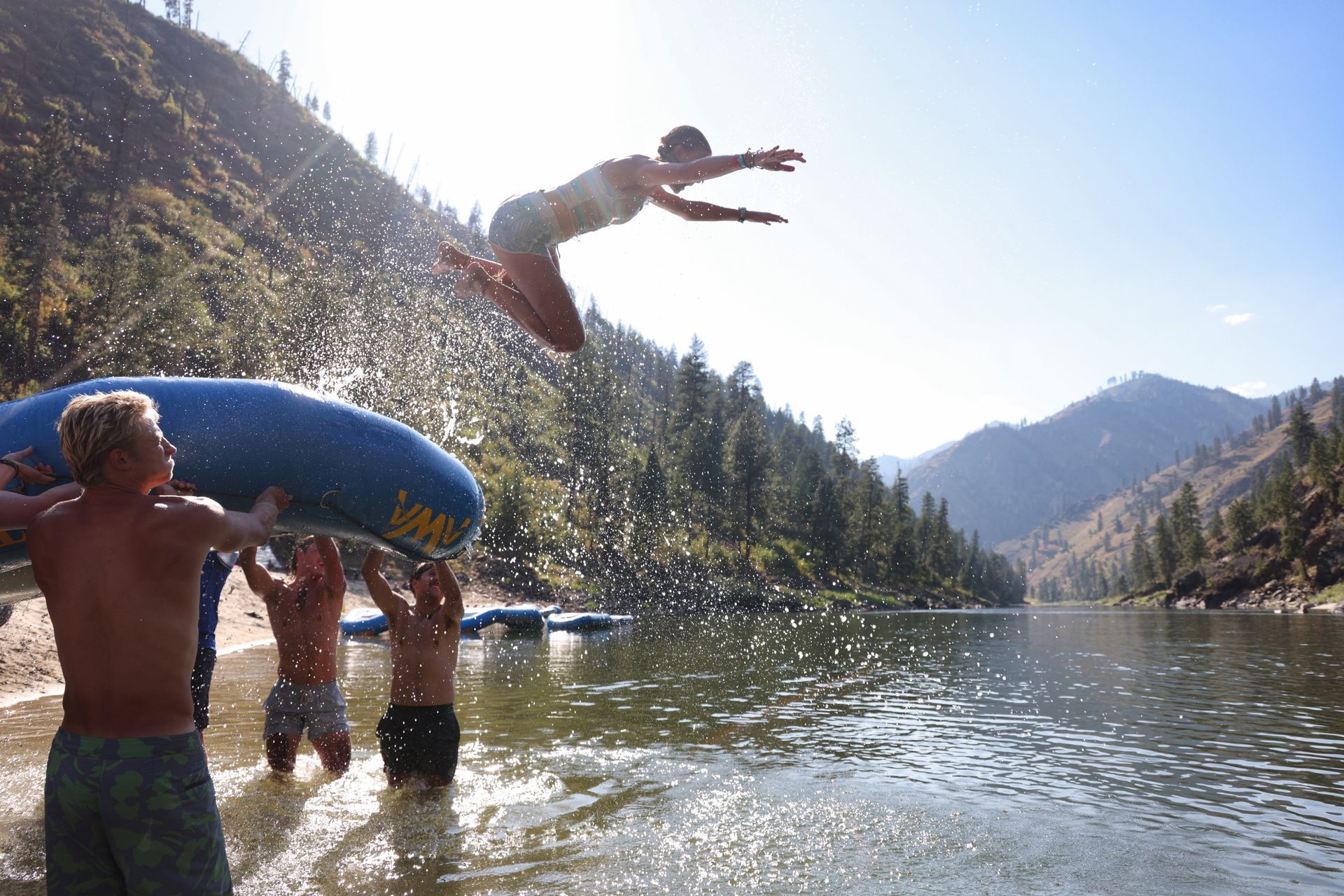 A rafter jumps from a raised inflatable kayak into the river