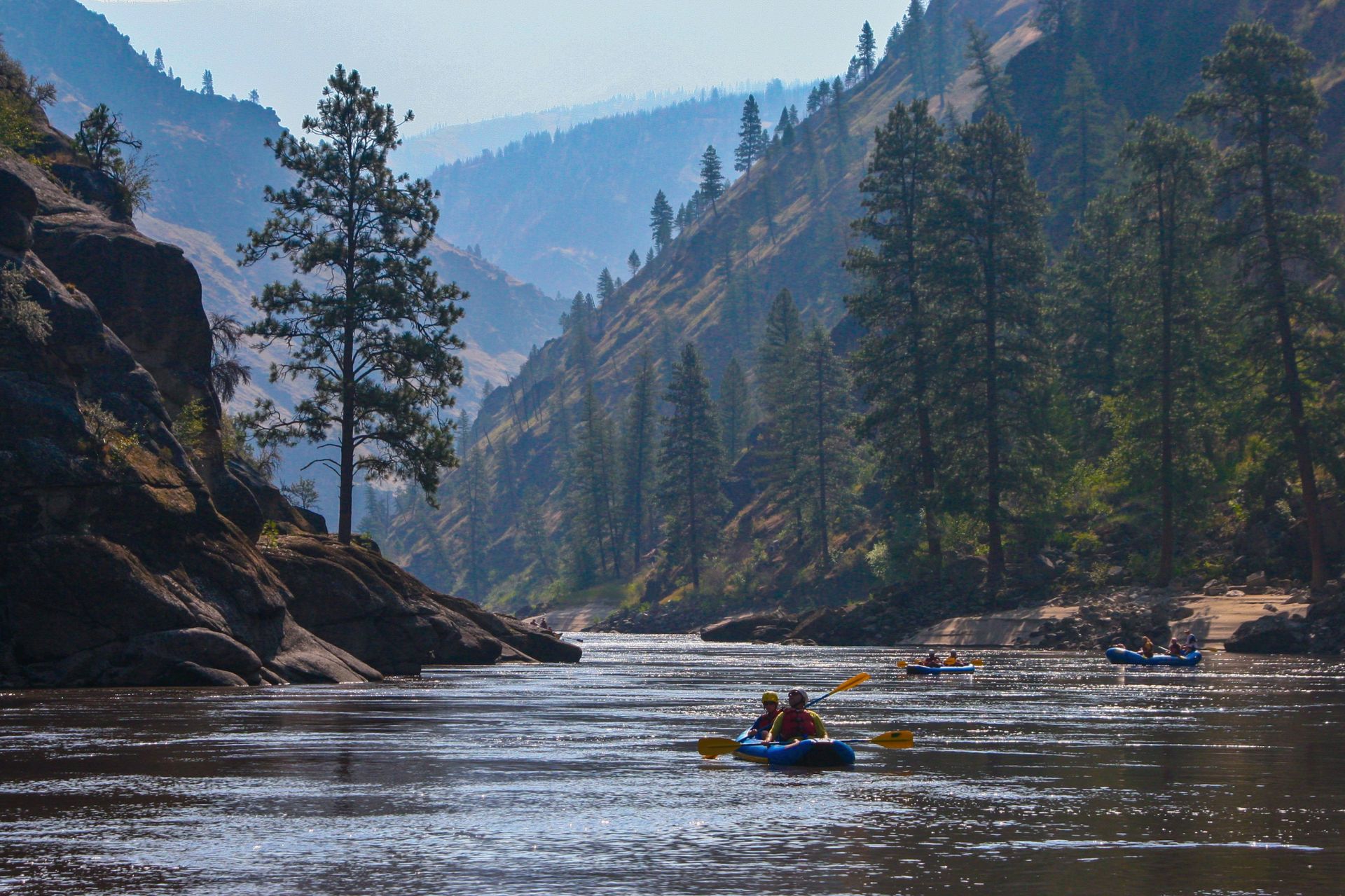 An inflatable kayak floats downstream between forested canyon walls