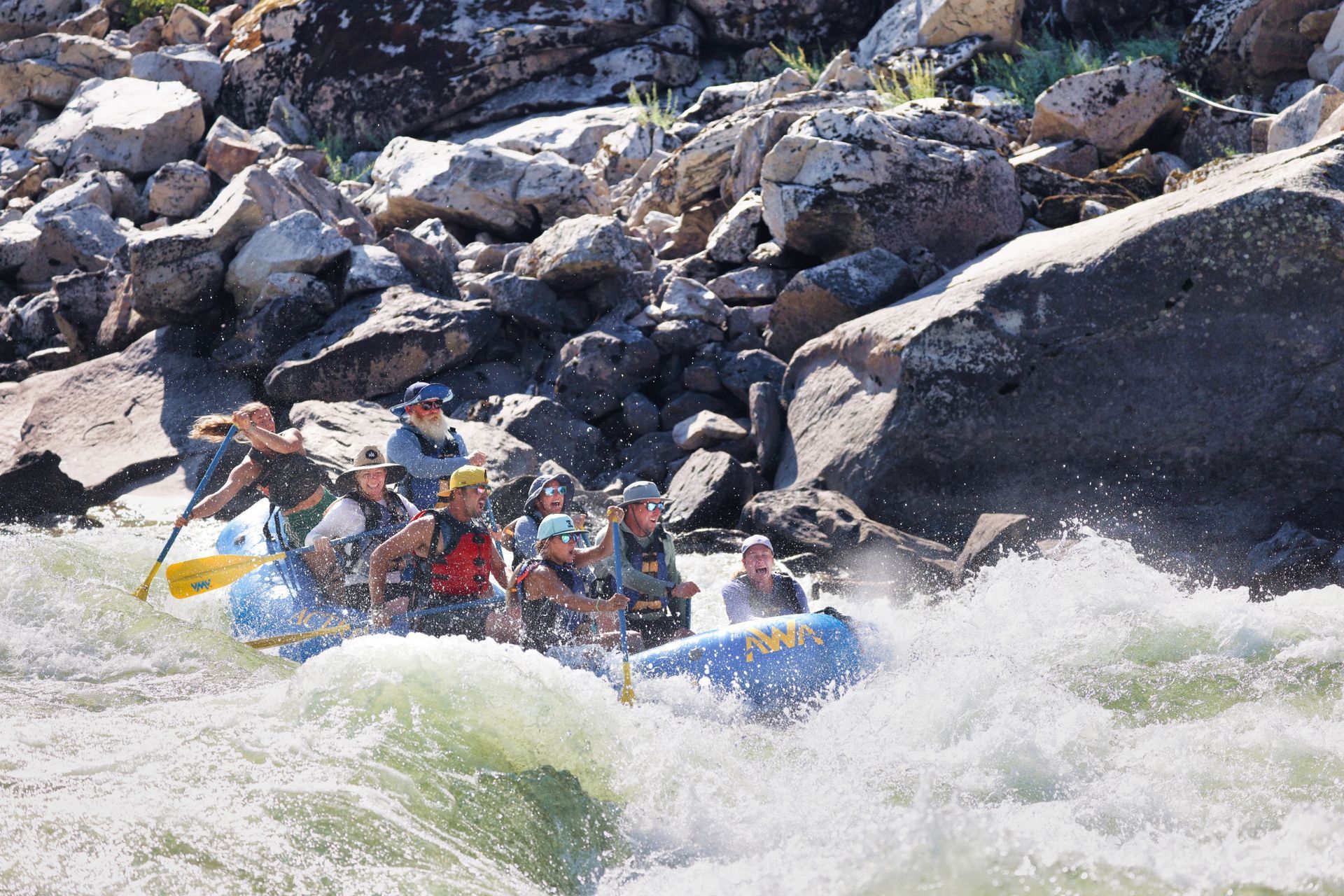 A blue raft enters a rapid beside a rocky canyon bank