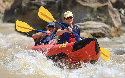Two rafters paddle an inflatable kayak through whitewater