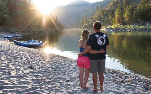 A couple standing beside the river at a beach camp in low sunlight